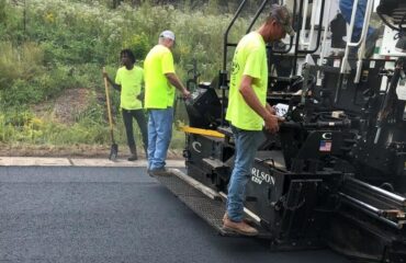 NCAT W10: BioMAG™ Carries 20% RAP Through 20 Million ESALs Three crew members stand on a paver placing a fresh asphalt mat at the NCAT Test Track.