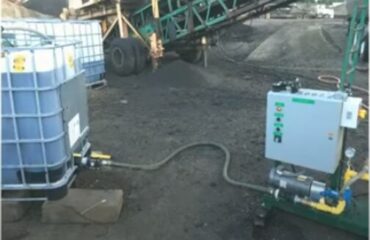 Rejuvenator tote connected by hose to a metering skid beside asphalt plant equipment in Emily, Minnesota.