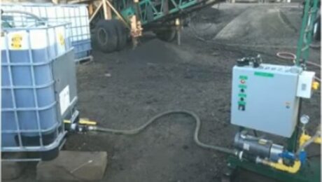 Rejuvenator tote connected by hose to a metering skid beside asphalt plant equipment in Emily, Minnesota.