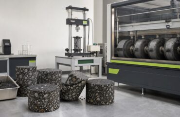 What the AASHTO PEAS Evaluation Shows for SIP-1111™ Asphalt specimens and laboratory testing equipment arranged around a roadway-materials workbench.